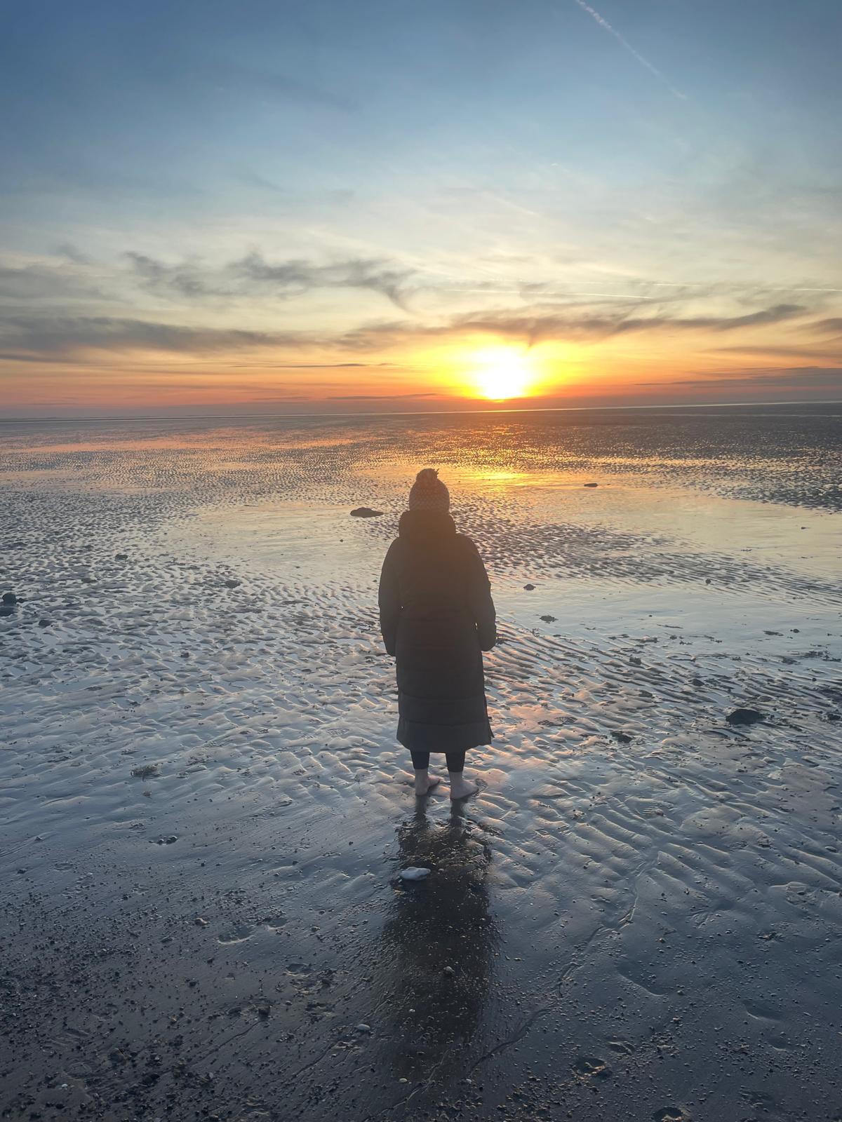 Gail standing at the water's edge at sunrise